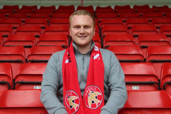 Ben Sadler sitting in a row of red seats at Bescot Stadium. He is wearing a red Walsall FC scarf.