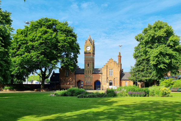 Red brick Victorian clock tower in Walsall Arboretum with grass in front, trees surrounding and blue sky