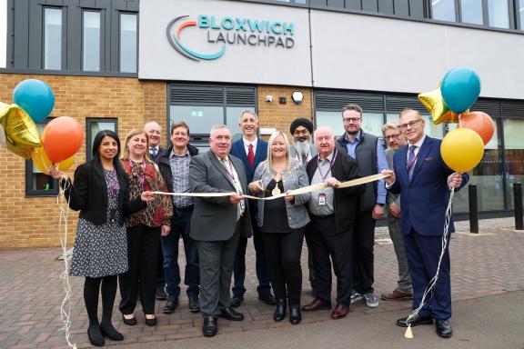 Walsall Mayor cutting a ribbon outside Bloxwich Launchpad, with a group of people holding balloons and smiling