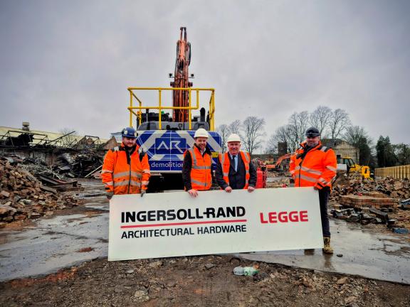 A group of people in high vis stand on a construction site holding a Legge Factory sign