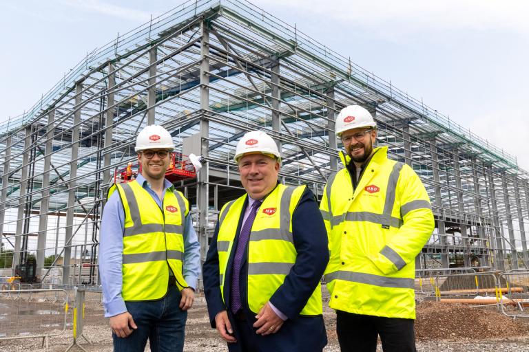 Three men wearing hi-vis standing in front of a large construction site