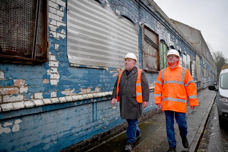 Two people in PPE walking along the side of the Legge building prior to demolition