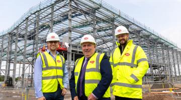 Three men wearing hi-vis standing in front of a large construction site