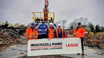 A group of people in high vis stand on a construction site holding a Legge Factory sign